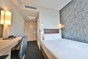 A hotel room with a bed, a desk with a chair, a mirror, and two wall-mounted lamps.