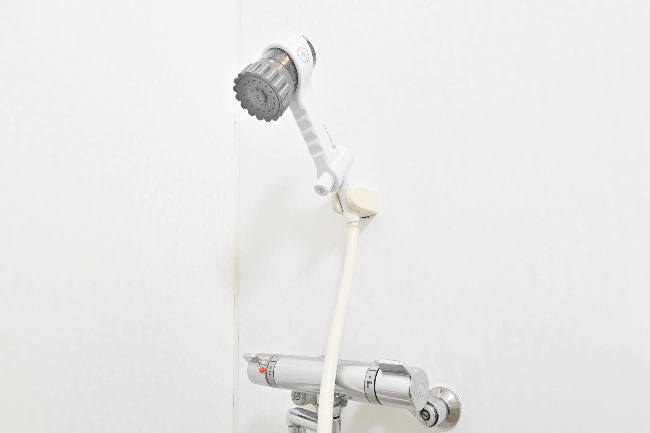 A showerhead with a white handle and a flexible hose attached to a wall-mounted faucet.