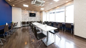 A conference room with a long table, chairs, a TV screen, and a brick wall with text. - Sanco Inn Yokkaichi Ekimae (Yokkaichi)