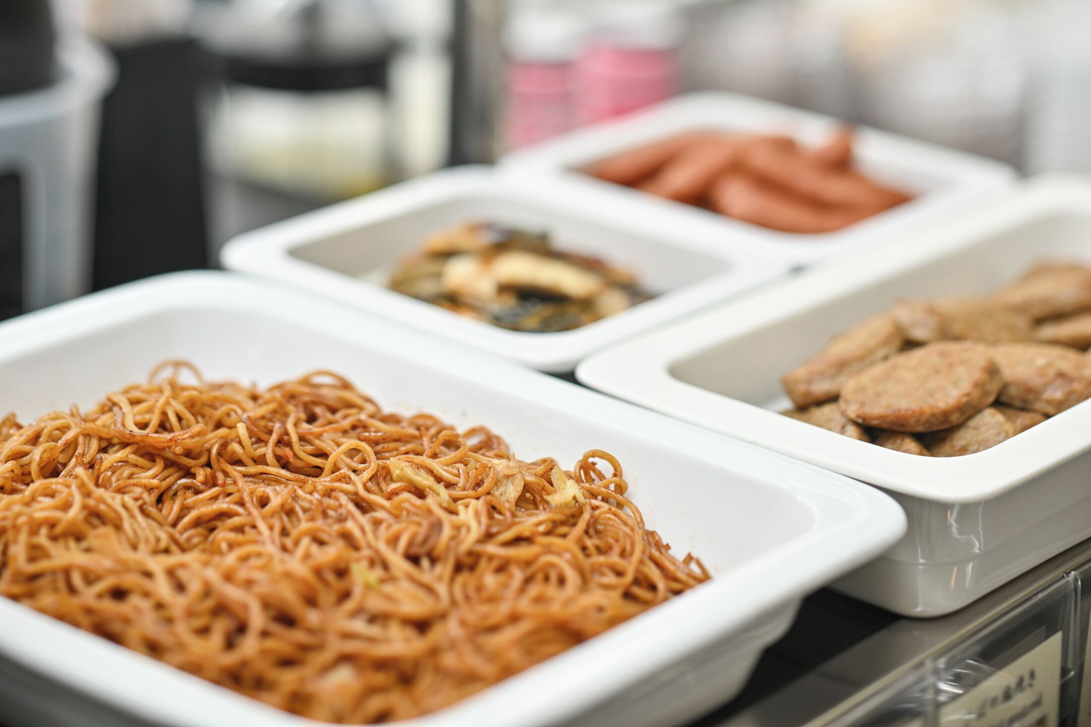 A buffet with various food items including noodles, sausages, and other dishes.