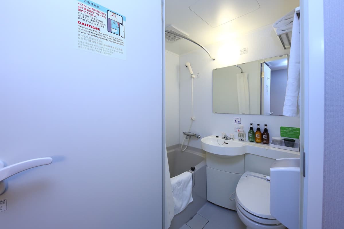 Une petite salle de bain avec des toilettes, un lavabo et une douche. Une serviette est accrochée au mur, et un panneau affiche des instructions.