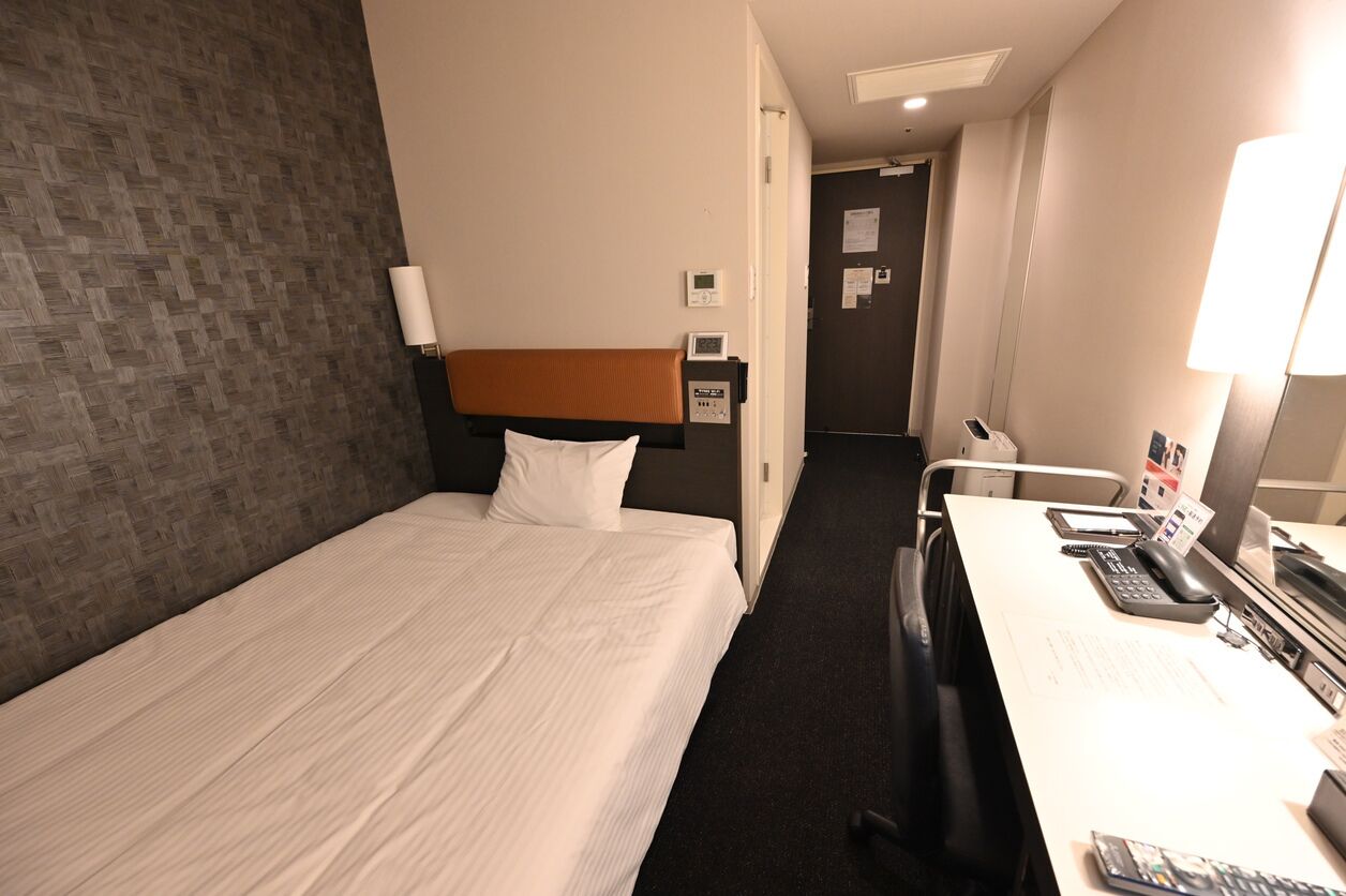 Une chambre d’hôtel comprenant un lit, un bureau avec un ordinateur, une chaise et une lampe.