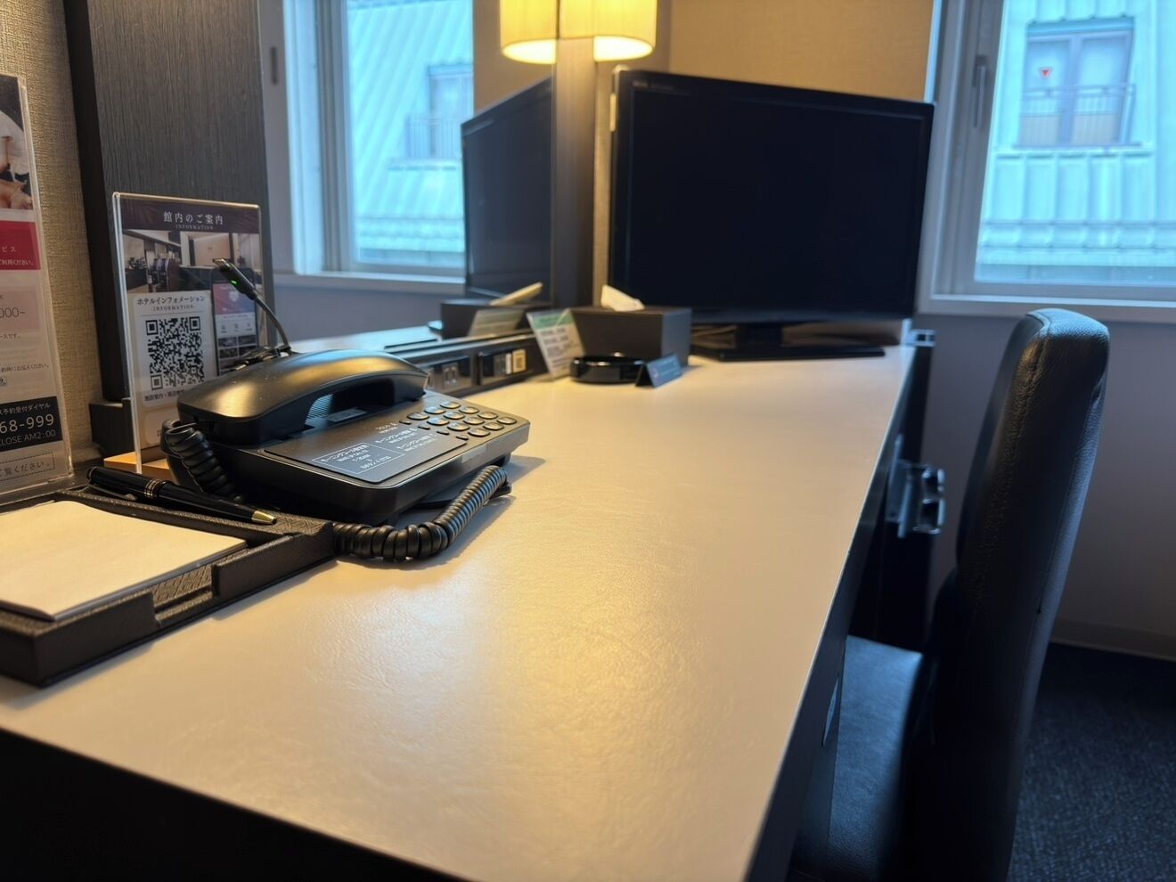 A hotel desk with a telephone, a notepad, and a QR code sign.