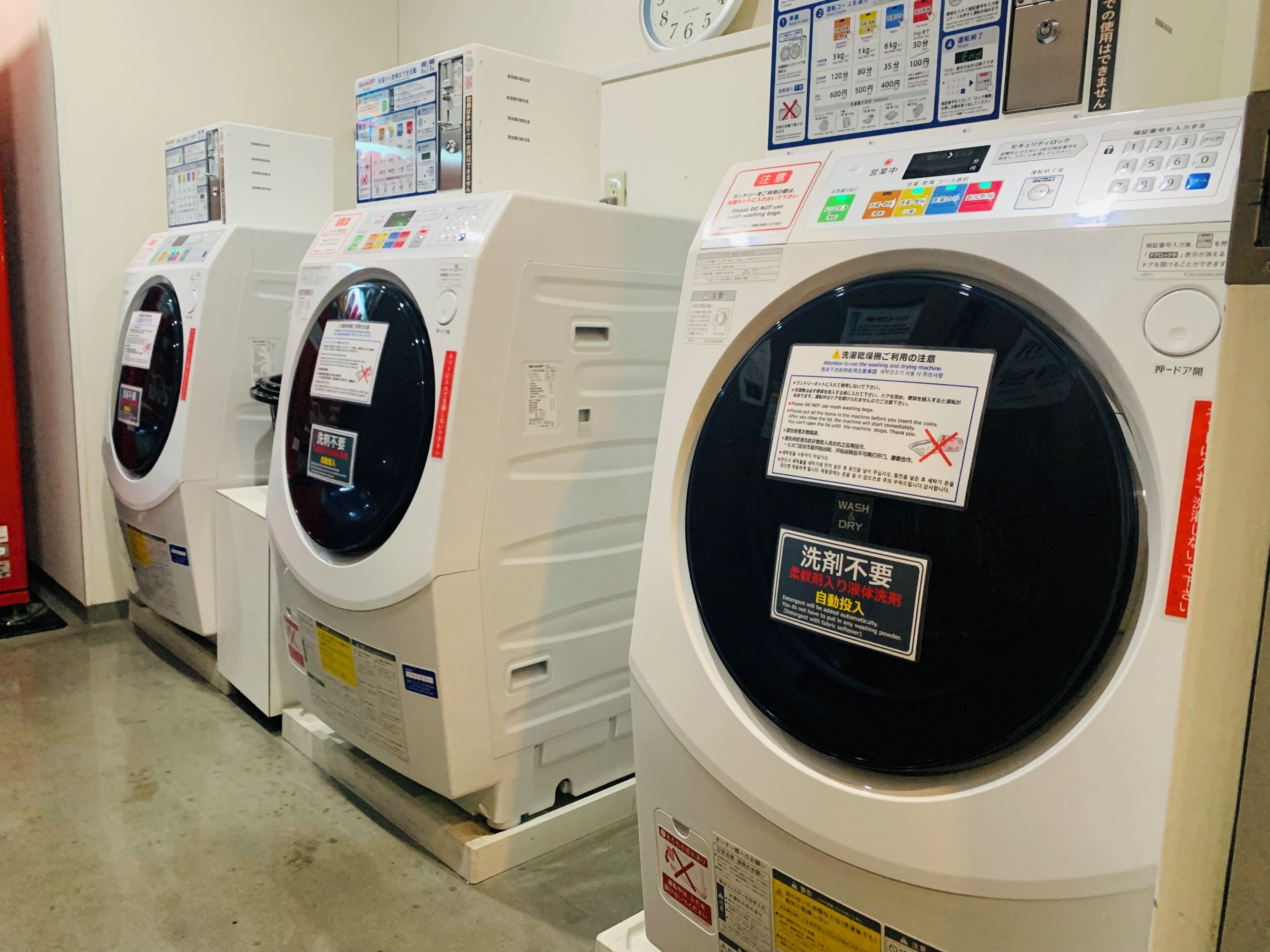 A row of white front-loading washing machines with control panels and safety instructions.