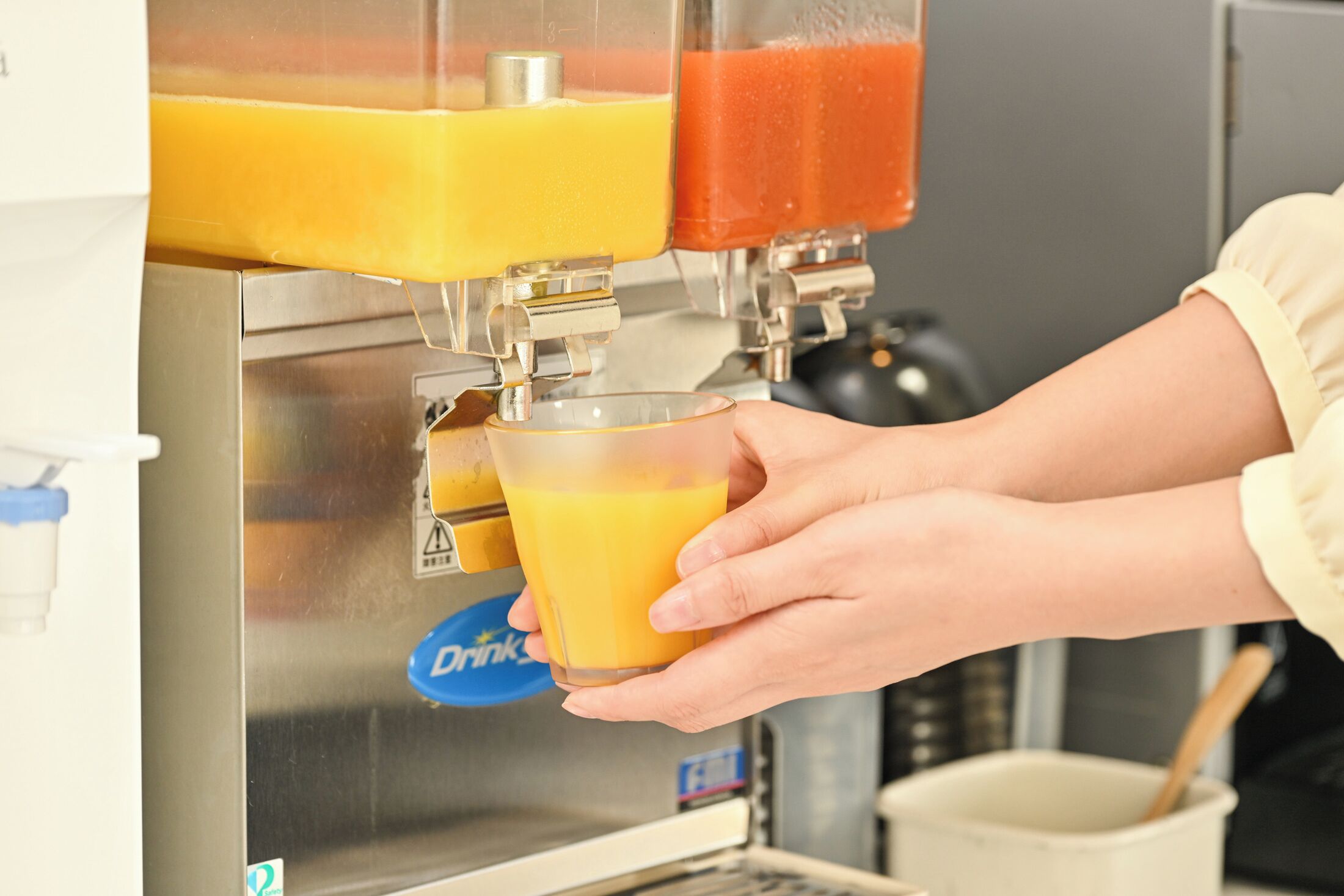 A person holding a glass of orange juice from a juice dispenser.