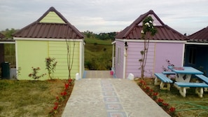 A pathway leading to three small, colorful cabins with benches and flower beds.