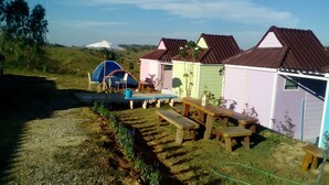 A campsite with wooden picnic tables, a tent, and small cabins with brown roofs. - Lovely Farm (Khao Kho)