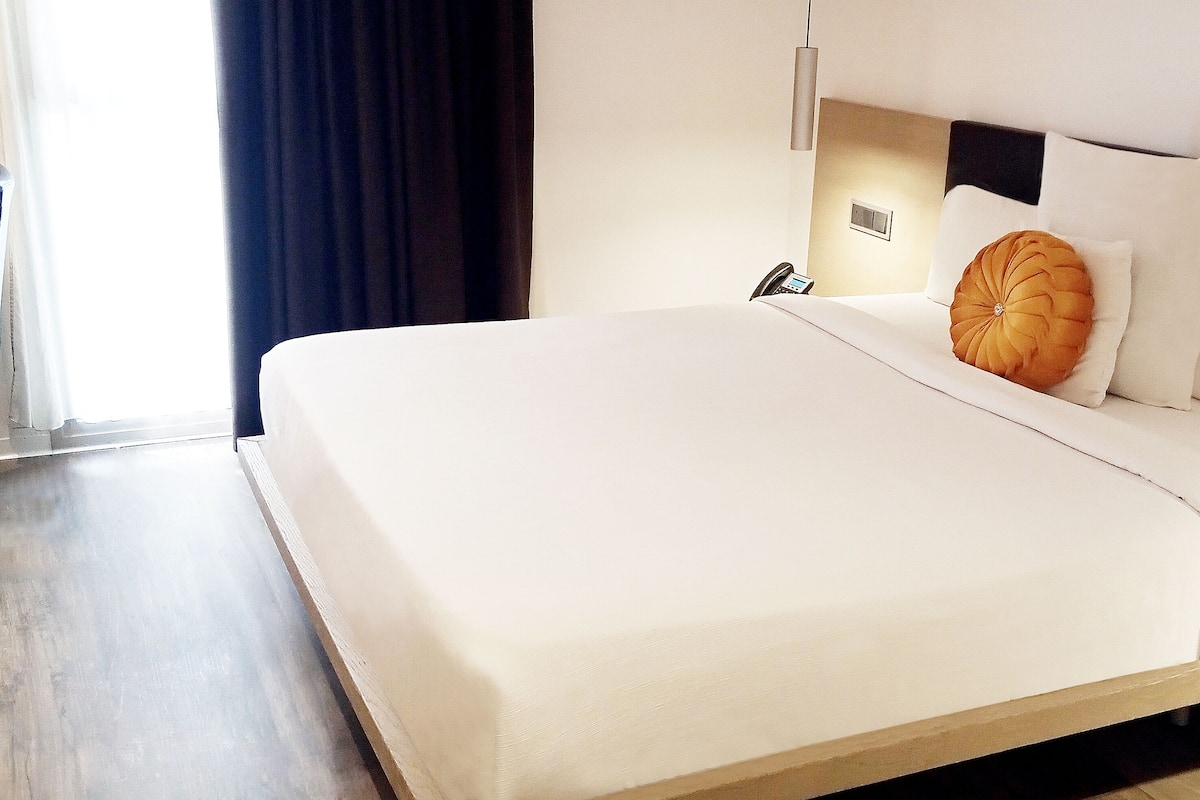 Hotellihuone, jossa on suuri sänky, yöpöytä, lamppu ja näkymä ulos.