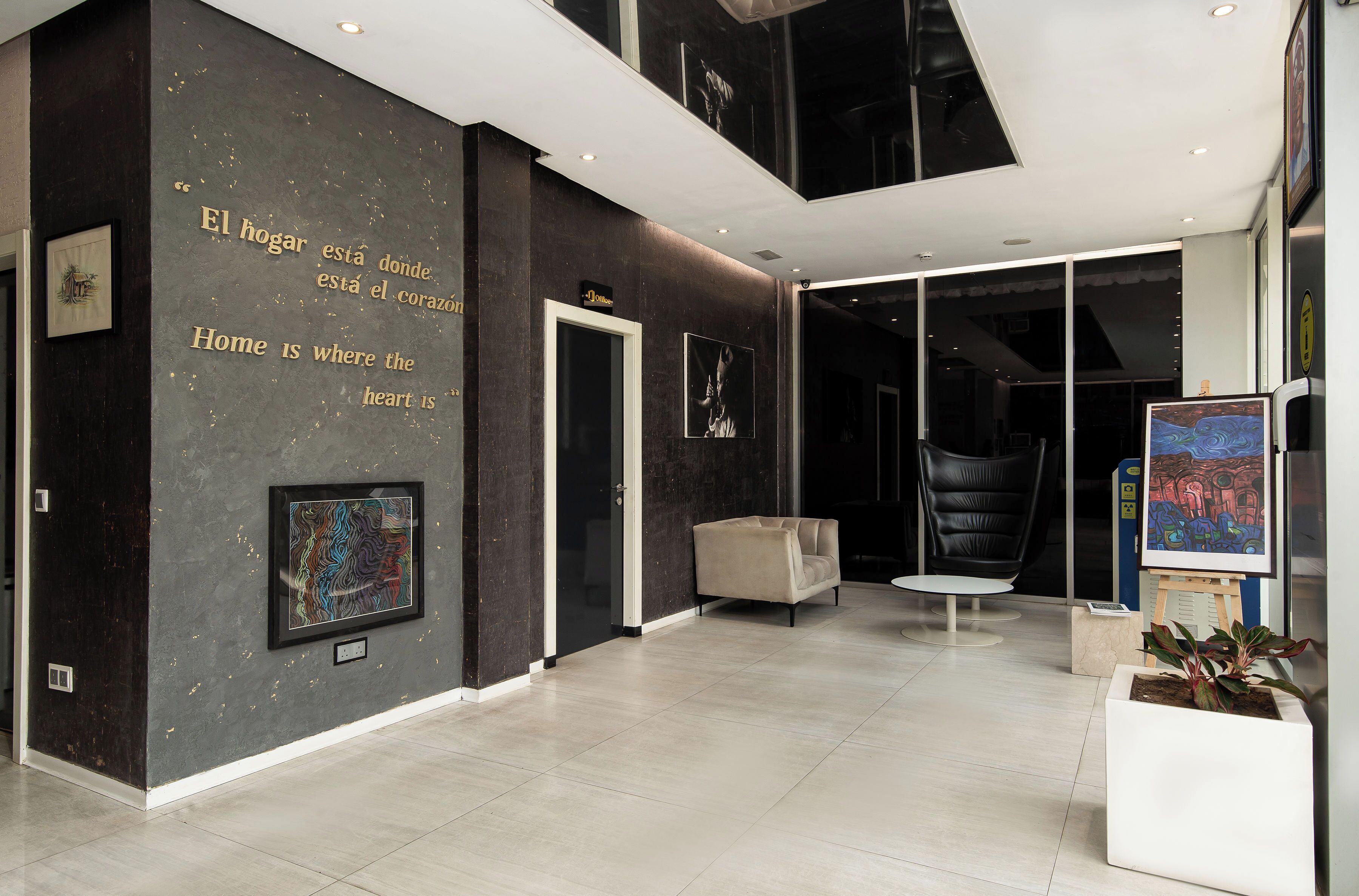 A modern interior with a dark wall featuring a quote in multiple languages, a framed artwork, a sofa, and a table.