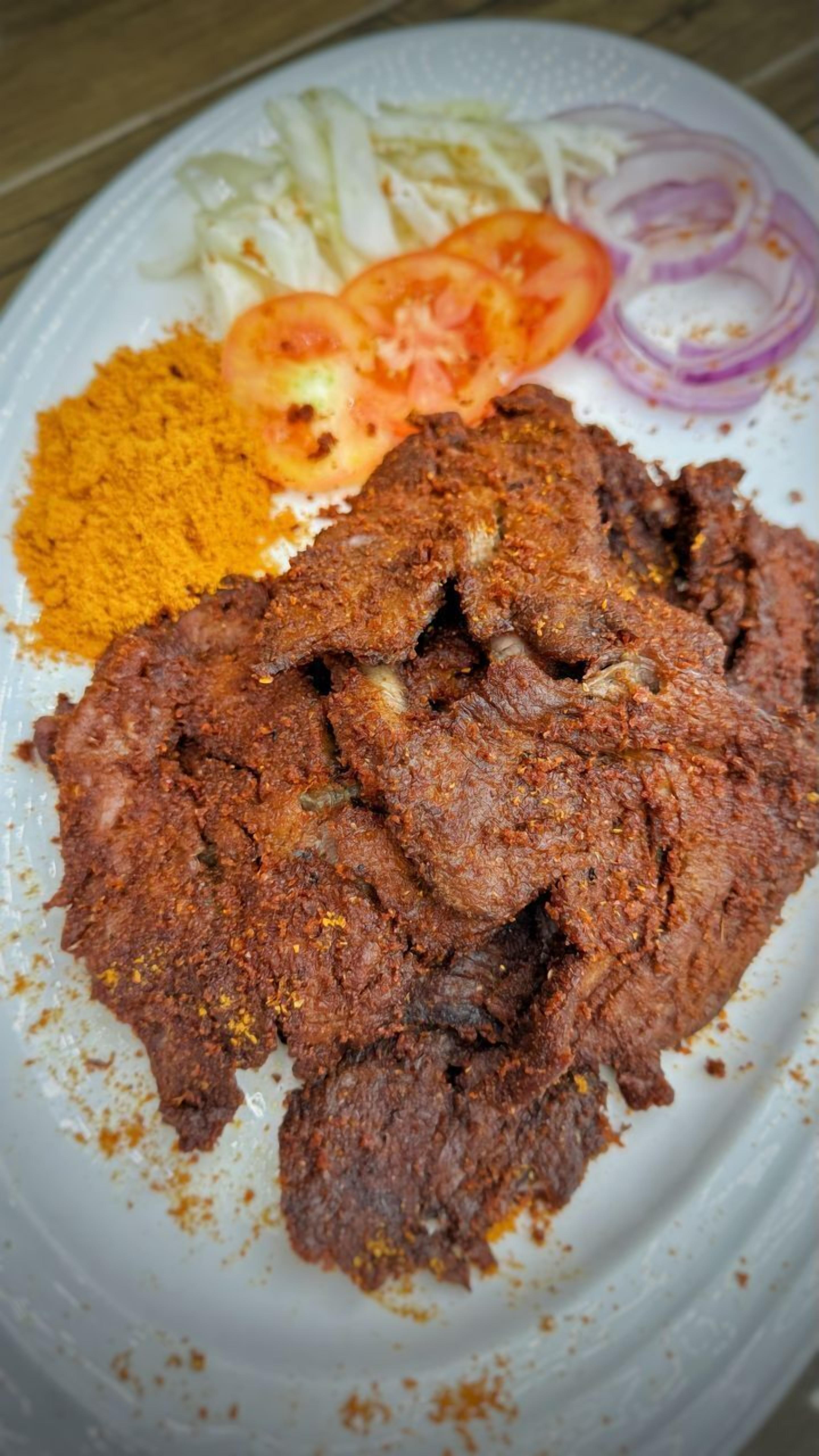 A plate with a serving of meat, sliced tomatoes, onions, and a yellow spice mix.