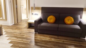 A modern living room with a dark sofa, two decorative pillows, a wooden bench, and a hallway leading to a bathroom. - SV Chrome (Abuja)