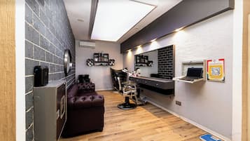 A modern hair salon with a dark brick wall, a leather sofa, a hair washing station, and a computer on a shelf.