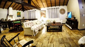 A cozy living room with a wooden ceiling, a white sofa, a coffee table, and a television on a stand. - Morada do Sol Guest House (Búzios)