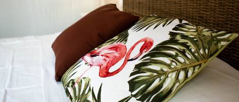 A bed with a white sheet, a brown pillow, and a floral pillow with a flamingo design.
