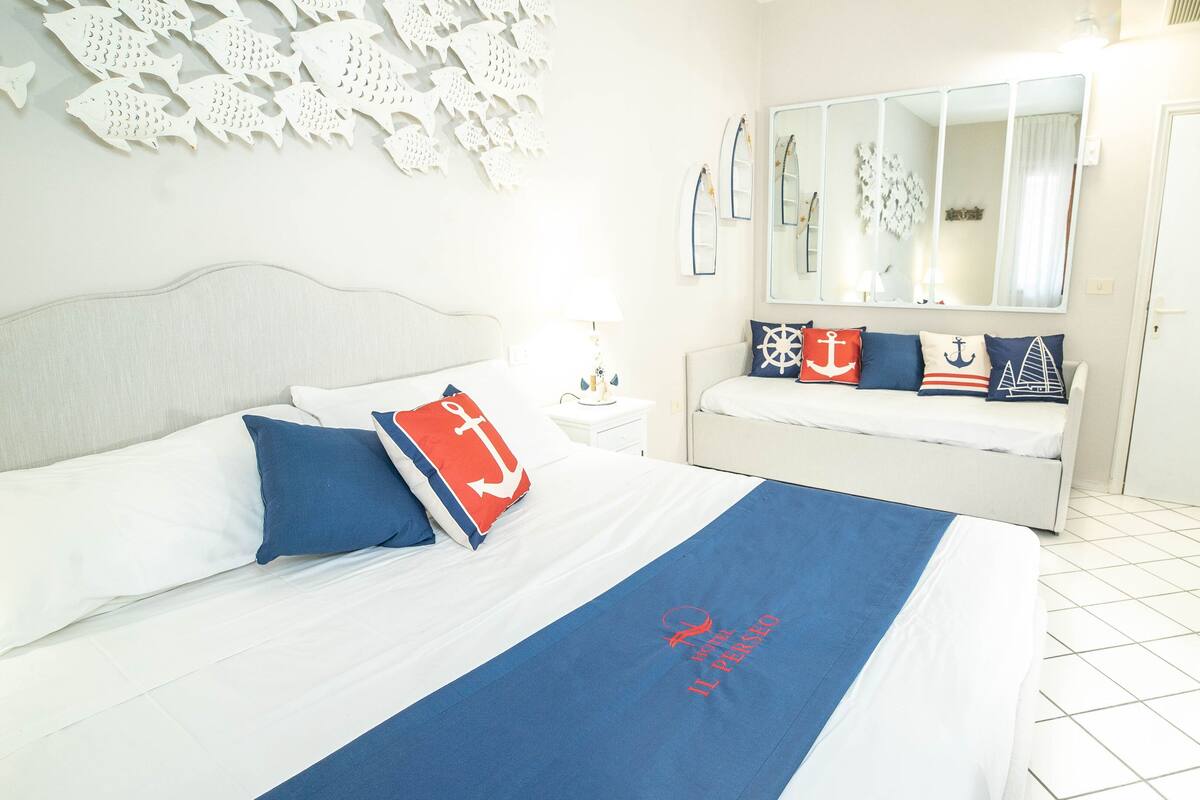 A hotel room with a bed, a nightstand, a dresser, and a large mirror.