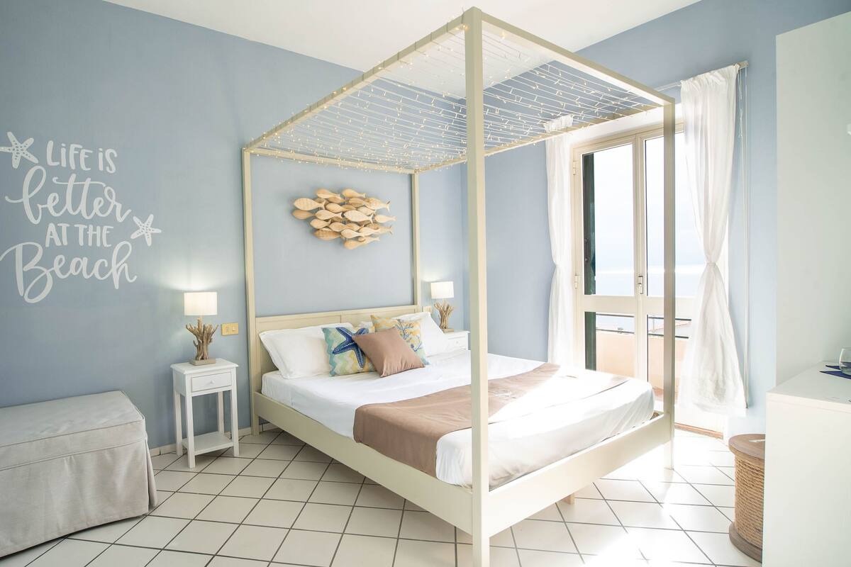 A bedroom with a four-poster bed, a small bedside table, a nightstand, a bench, and a wall with a decorative fish wall art and a motivational quote.