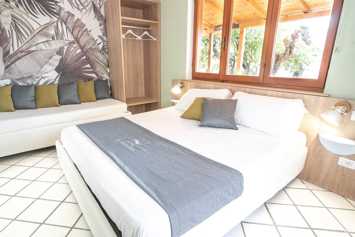 A bedroom with a bed, a sofa, a wardrobe, and a window with a view of trees.