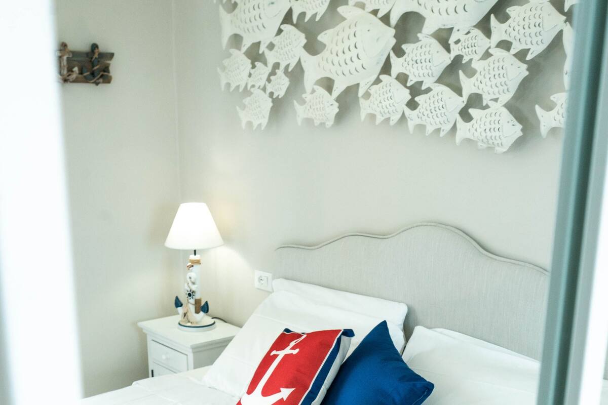 A neatly made bed with white and blue bedding, a nightstand with a lamp, and a wall decoration.