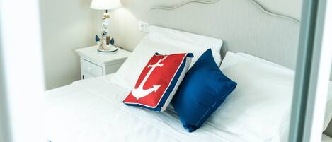 A neatly made bed with white and blue bedding, a nightstand with a lamp, and a wall decoration.