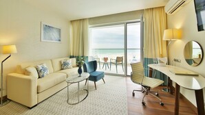 A hotel room with a sofa, a chair, a small table, a desk, and a view of the beach. - MARITIM Paradise Blue Hotel & Spa (Albena)
