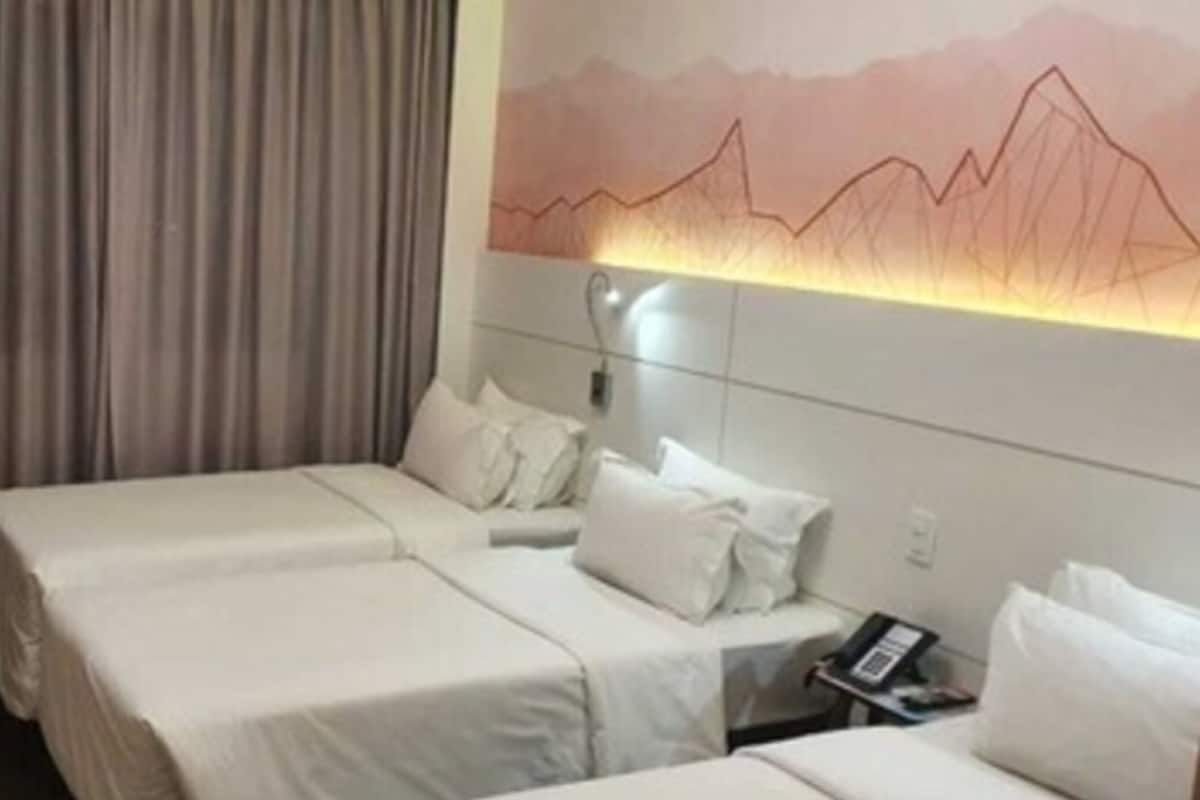 A hotel room with two beds, a desk, a chair, and a wall-mounted lamp.