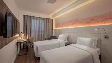 Habitación de hotel con dos camas, un escritorio, una silla, un televisor y una lámpara fijada a la pared.