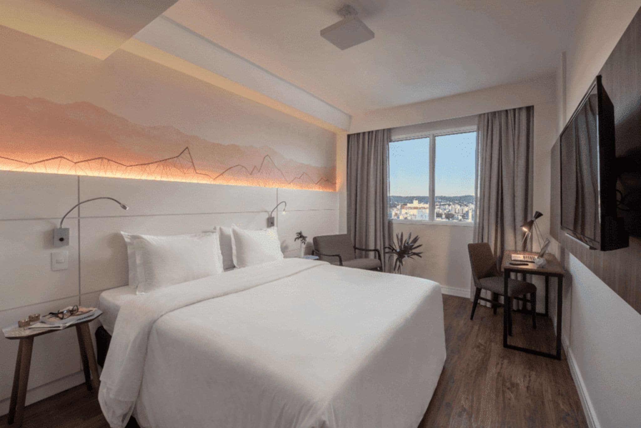 Une chambre d’hôtel avec un grand lit, un bureau avec une chaise, une télévision et une fenêtre donnant sur la ville.