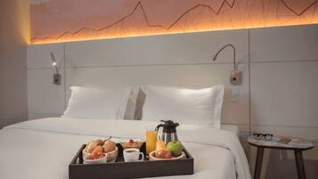 Ein Hotelzimmer mit einem ordentlich bezogenen Bett, einem Tablett mit Frühstücksgegenständen und einer wandmontierten Lampe.