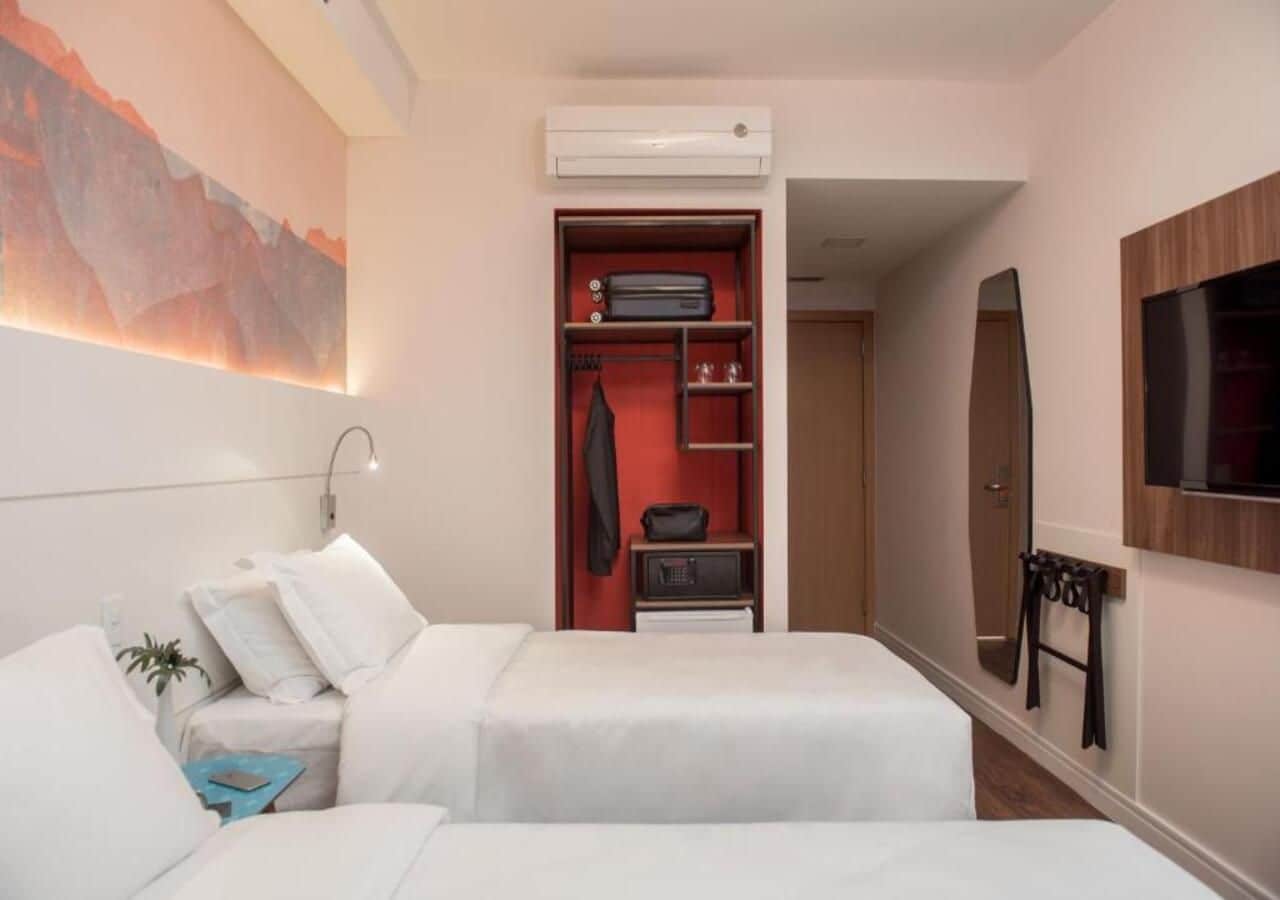 A hotel room with two beds, a wardrobe, a mirror, and a TV.