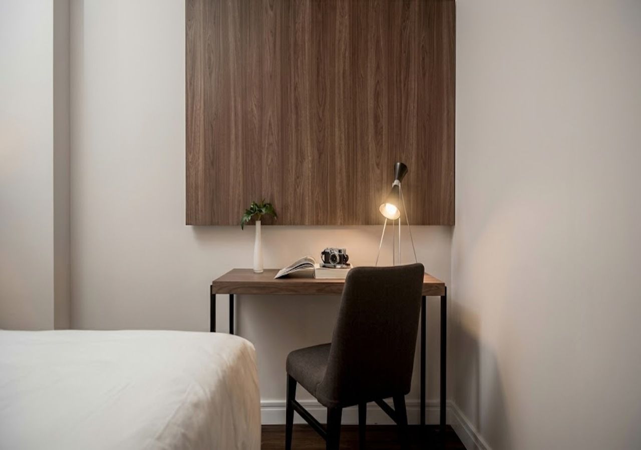 A room with a bed, a desk with a chair, a lamp, and a plant.