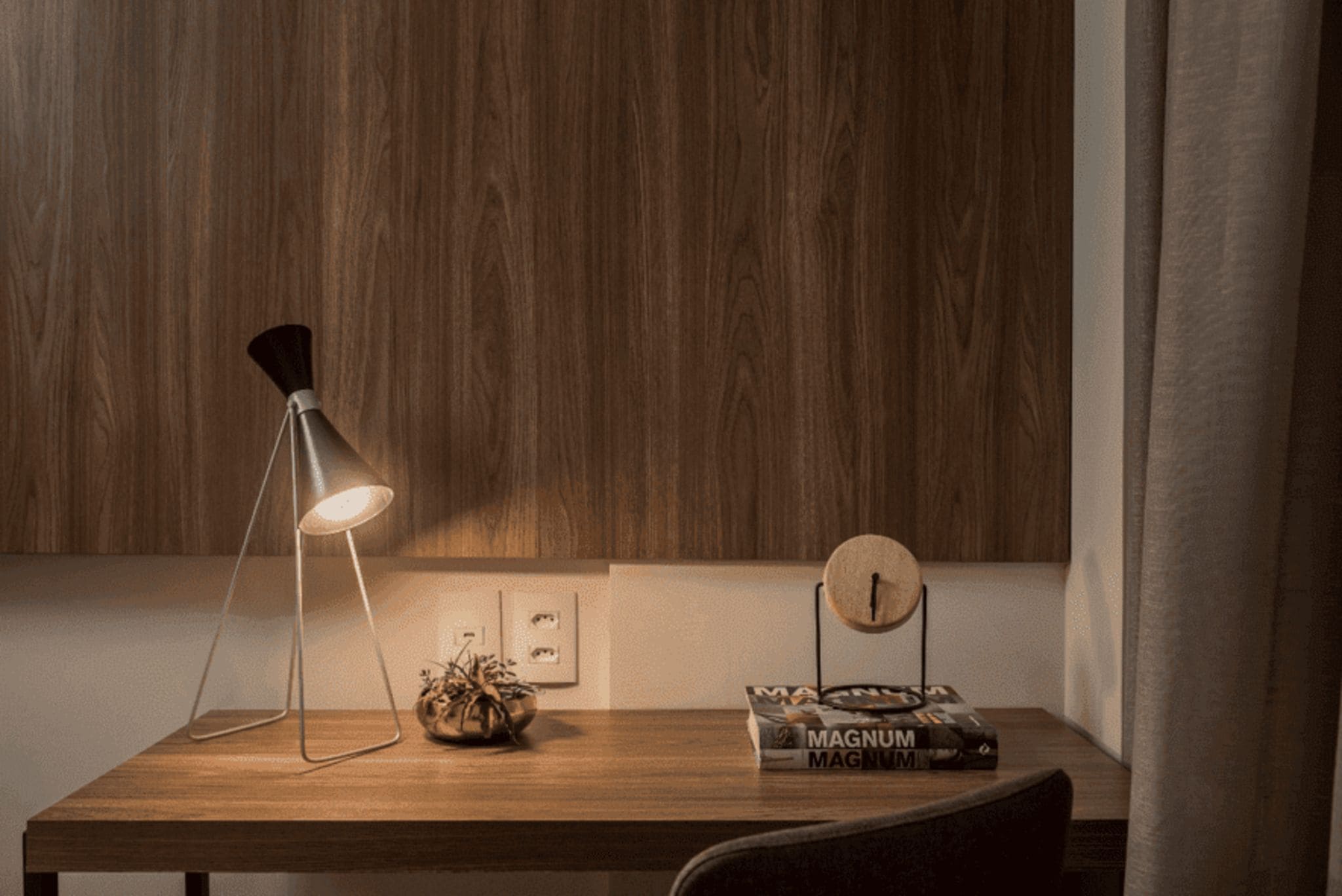 Un bureau en bois, avec une lampe de bureau, une horloge et un livre intitulé « MAGNUM ».