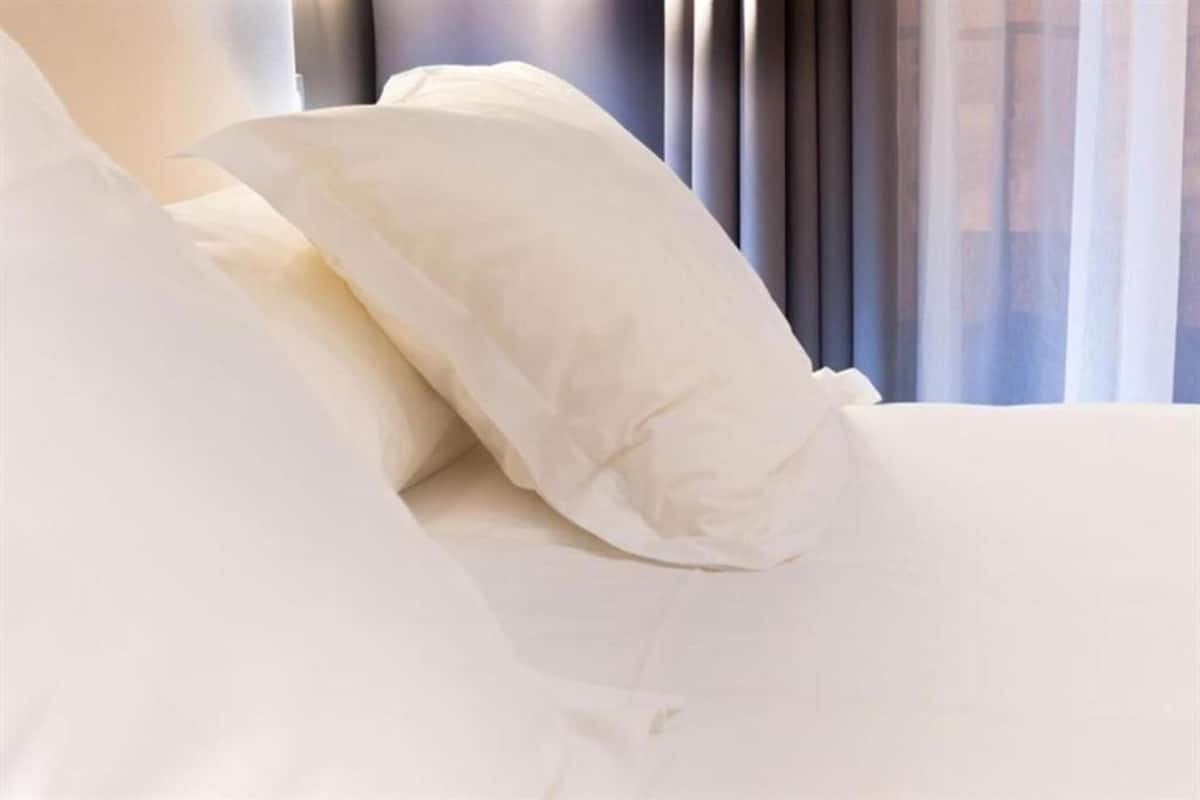 A bed with white bedding and a window with sheer curtains.