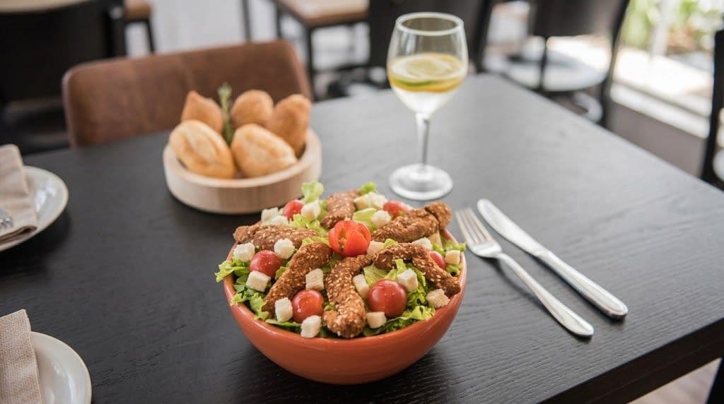 A table with a bowl of salad, a glass of white wine, and a plate of bread.