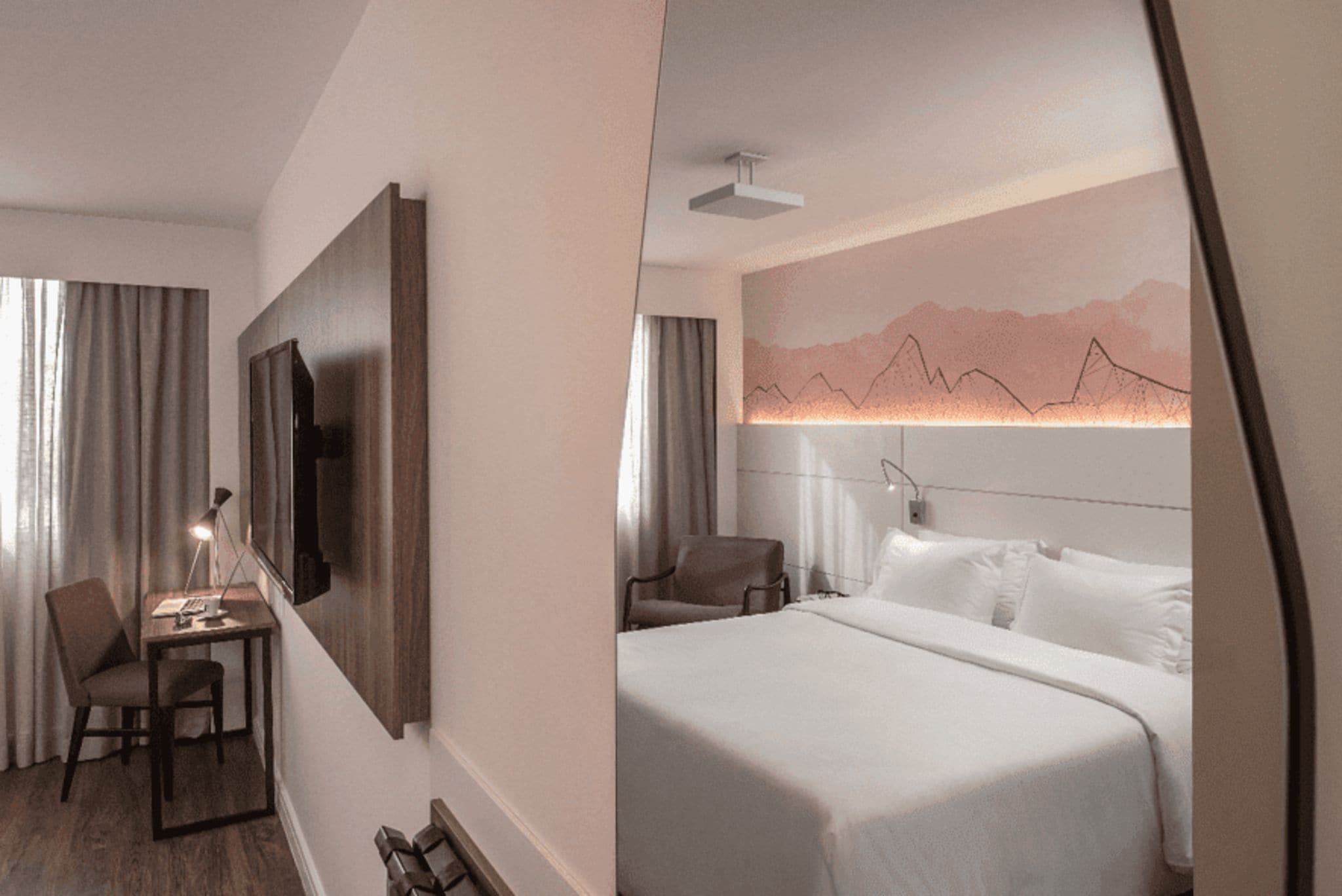 Habitación de hotel con escritorio, silla, cama y televisor de pared.