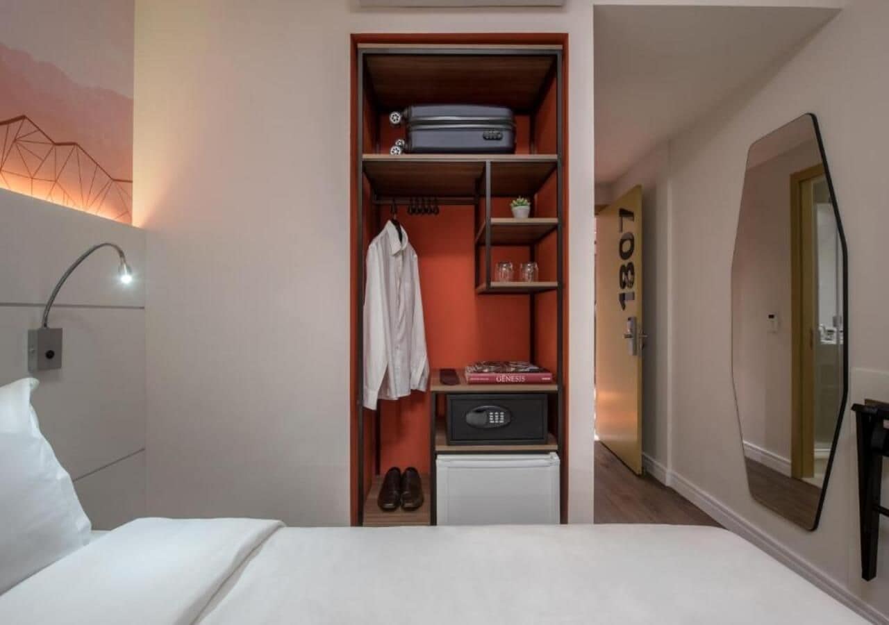 Une chambre d’hôtel comprenant un lit, une armoire avec des étagères, un miroir et une porte donnant sur une autre pièce.