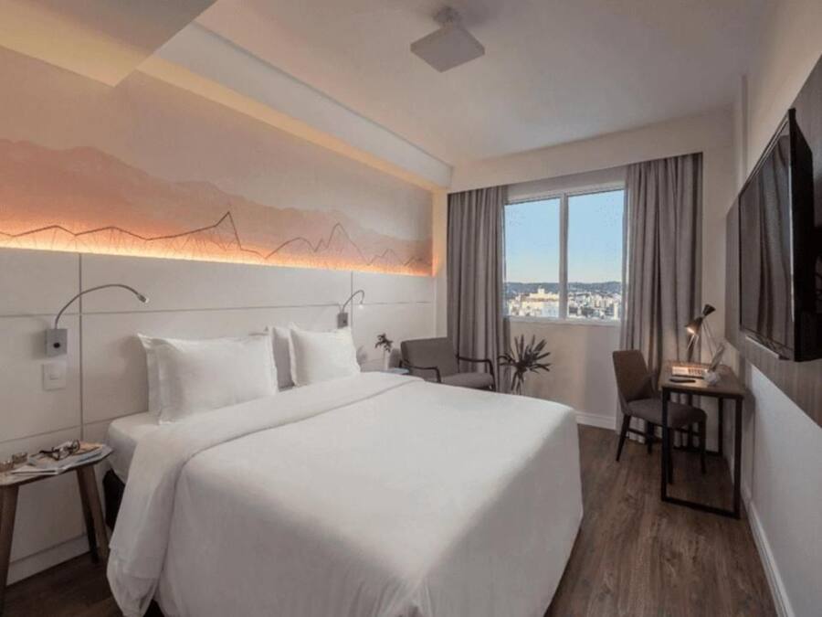 Habitación de hotel con una cama grande, un escritorio, una silla, vista a la ciudad y un diseño de montaña en la pared.