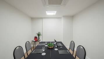 Ett konferensrum med ett långt bord, fyra stolar, en bärbar dator, en växt och ett litet bord med ett rött föremål och en växt.