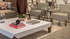 Ein stilvoller Lounge-Bereich mit weißem Couchtisch, mehreren Sesseln, einer großen Pflanze und einem geometrischen Wanddekor.