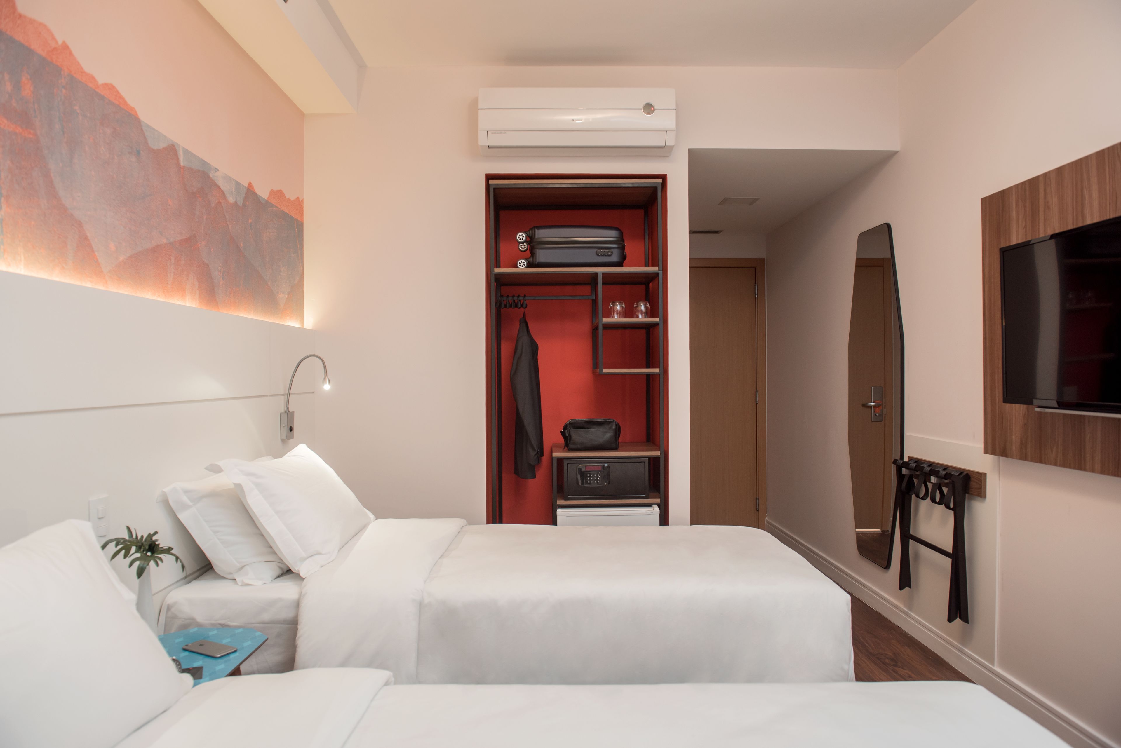 A hotel room with two beds, a wardrobe, a TV, and a painting on the wall.