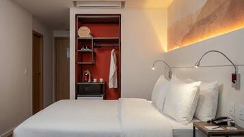 A hotel room with a bed, bedside table, and a built-in wardrobe with shelves.