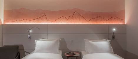 A hotel room with two beds, a small table, and a wall-mounted light fixture.