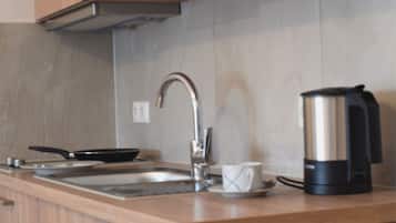 A modern kitchen with a stainless steel sink, a coffee maker, and a frying pan on the counter.