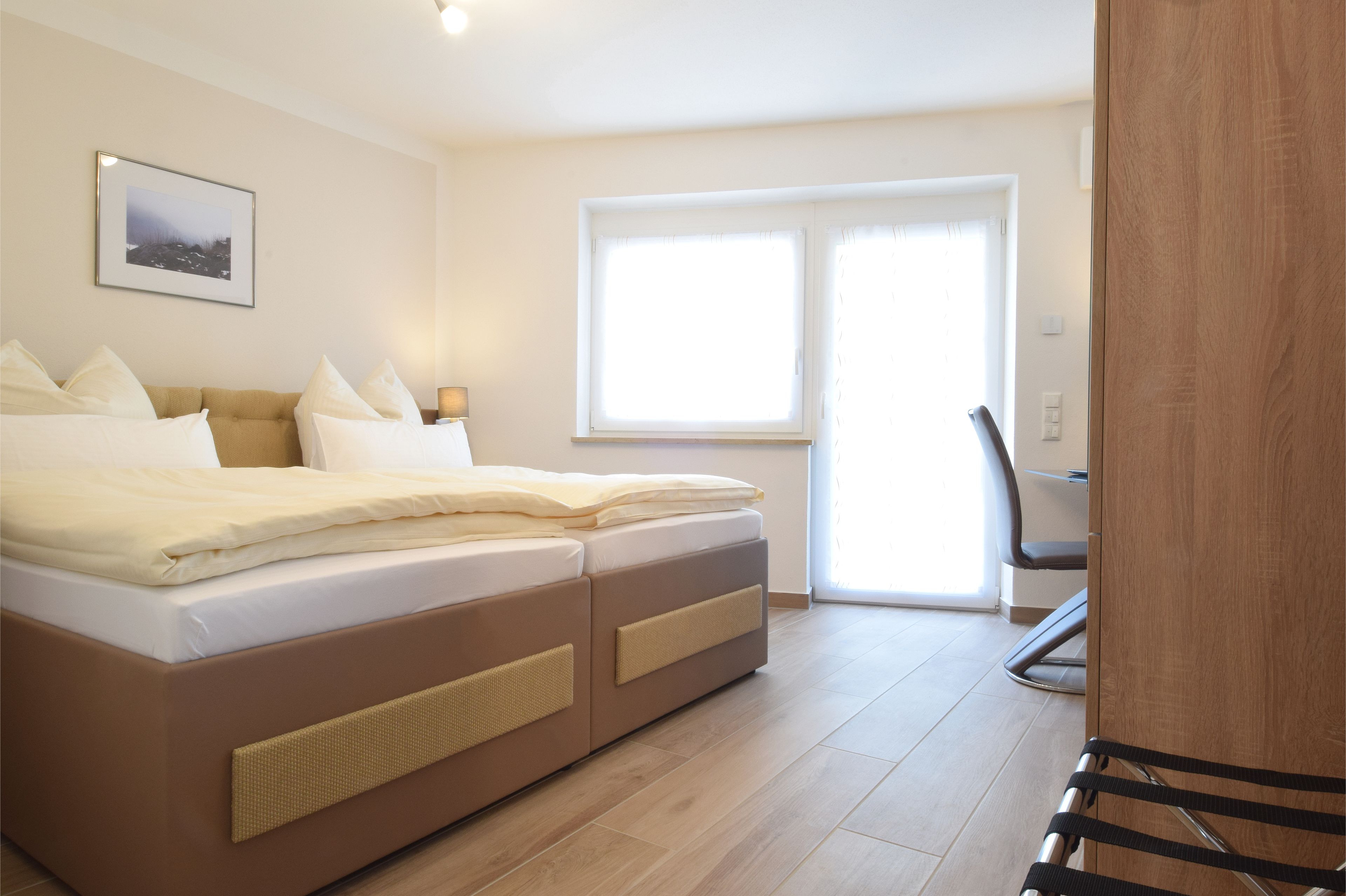 A bedroom with a bed, a chair, a desk, and a window.