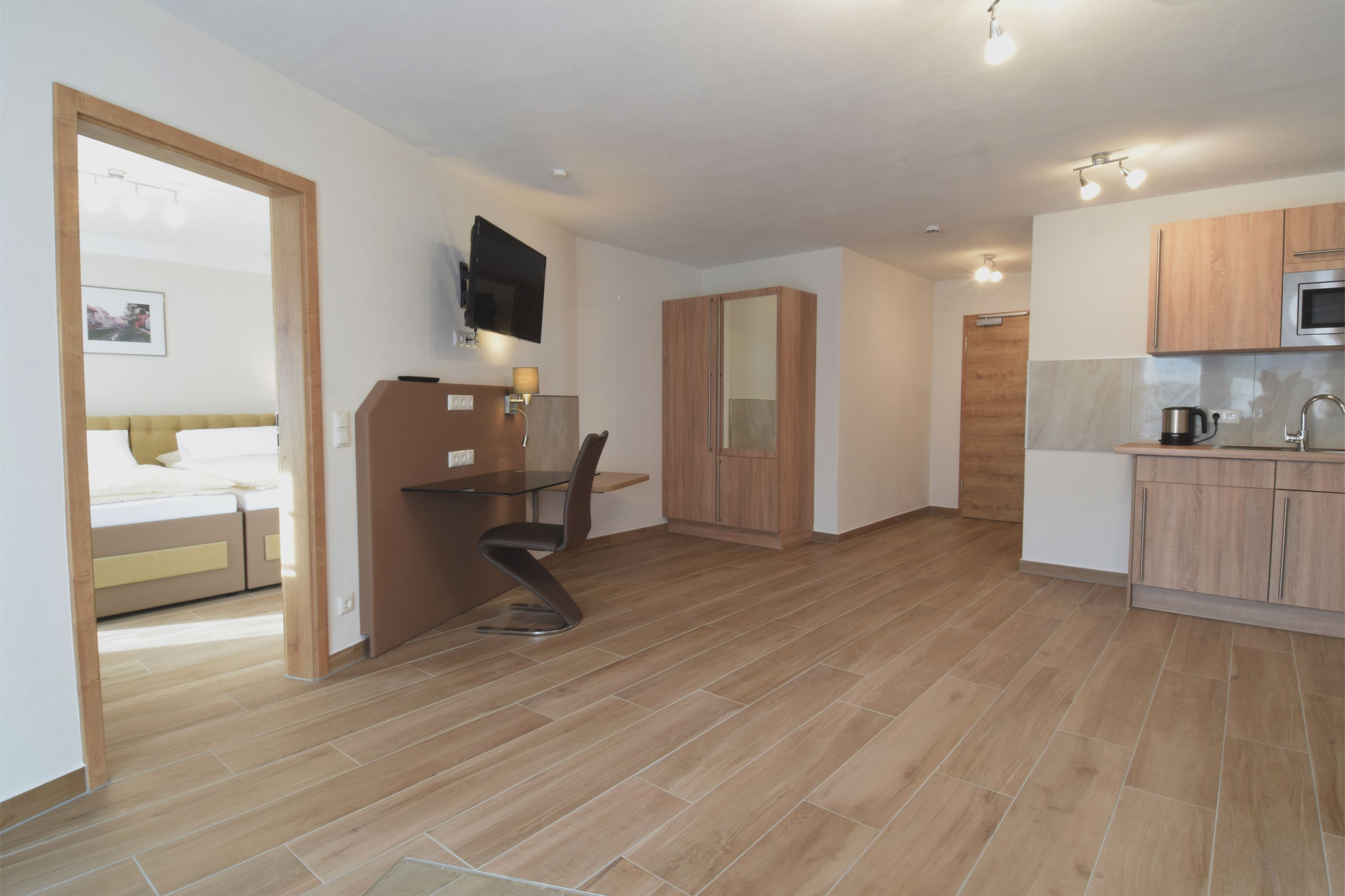 A modern hotel room with a bed, a desk, and a kitchenette.