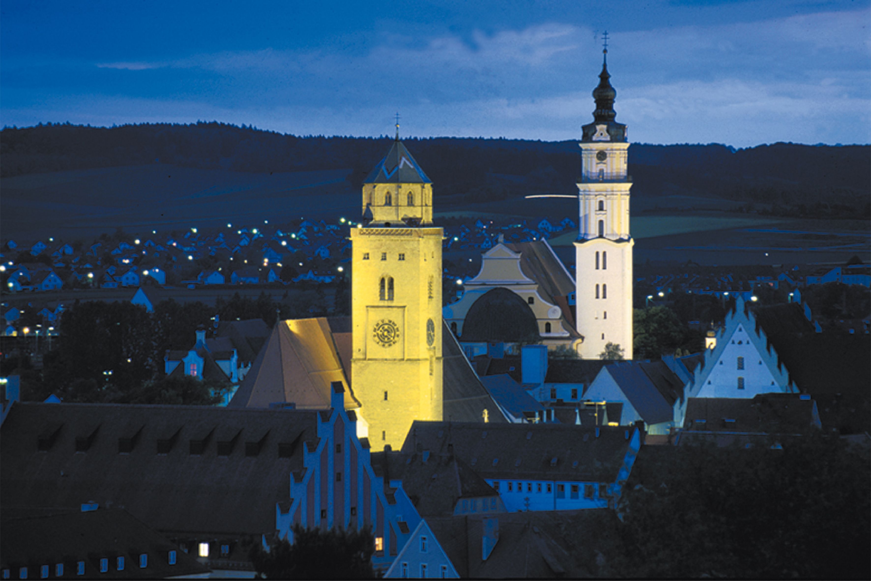 Eine historische Stadt mit markanten Türmen und einer Kirche, umgeben von traditioneller Architektur und einer kleinstädtischen Struktur.