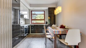 A modern kitchen with a large window, a dining area with a striped tablecloth, and a white chair. - Rent a Flat Apartments - Torunska 18 (Gdansk)