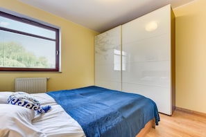 A bedroom with a bed, a window with blinds, a radiator, and a wardrobe. - Rent a Flat Apartments - Torunska 18 (Gdansk)