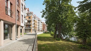 A multi-story residential building with balconies, a paved walkway, and a grassy area with trees. - Rent a Flat Apartments - Torunska 18 (Gdansk)