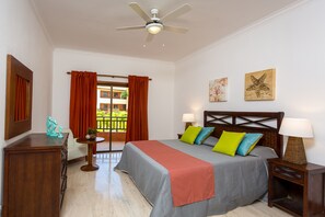A hotel room with a bed, two bedside tables, a ceiling fan, a window with curtains, and artwork on the walls.