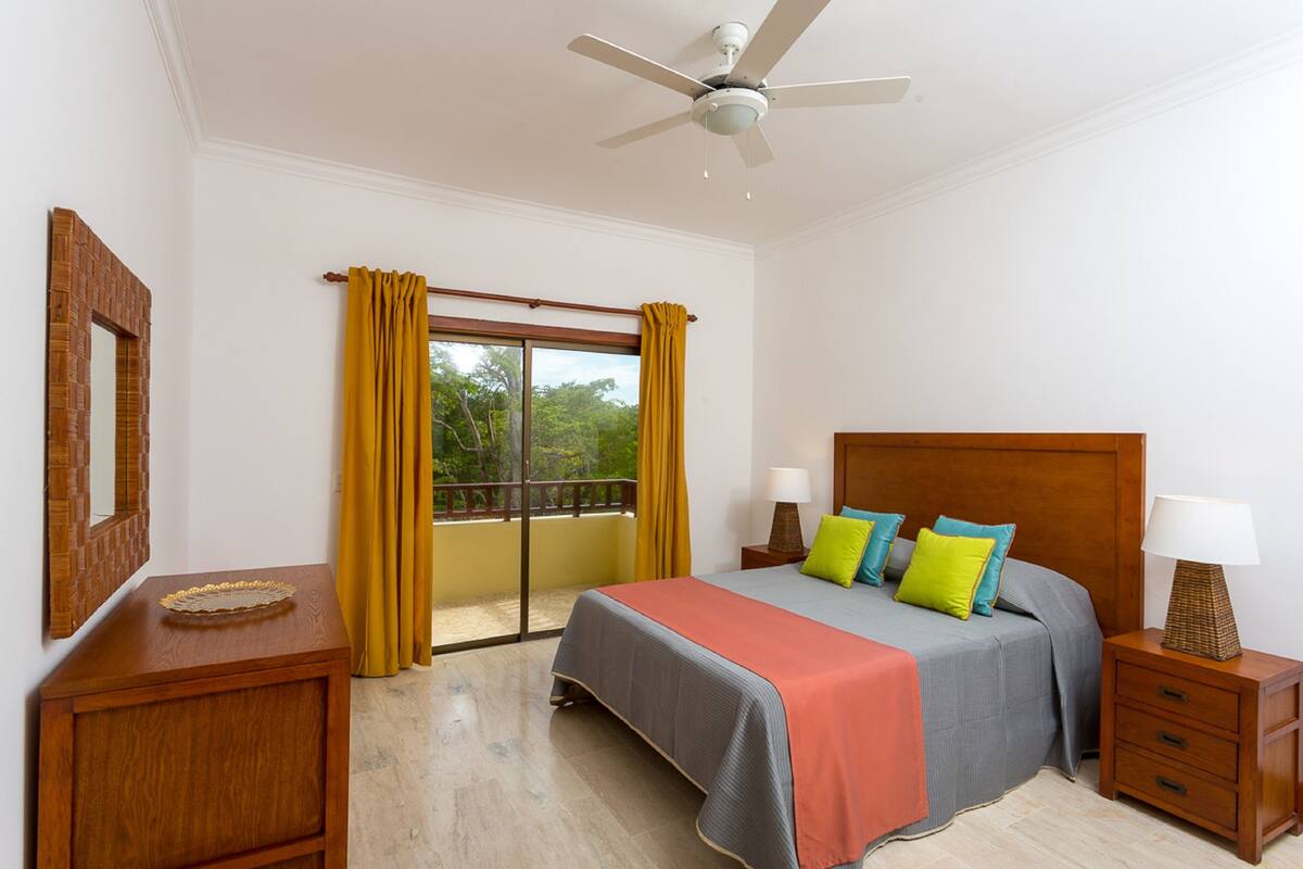 A hotel room with a bed, nightstands, a mirror, and a balcony with curtains.